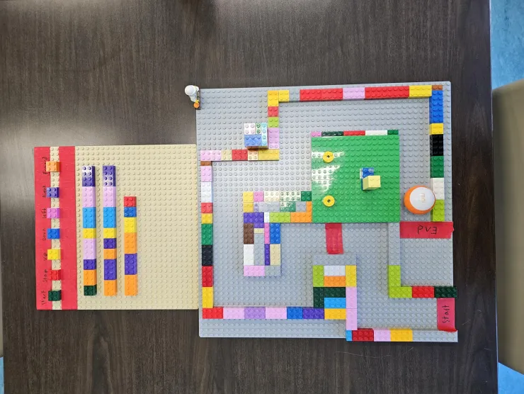 Small LEGO board with movement directions. Then large Lego board with maze and small round blue and white robot at the start.