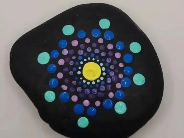 a black rock with a circular set of designs painted in shades of blue and purple