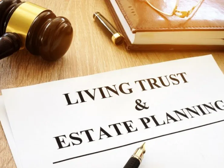 A piece of paper with the text living trust & estate planning. laying beside it is a brown gavel and a notebook and pen