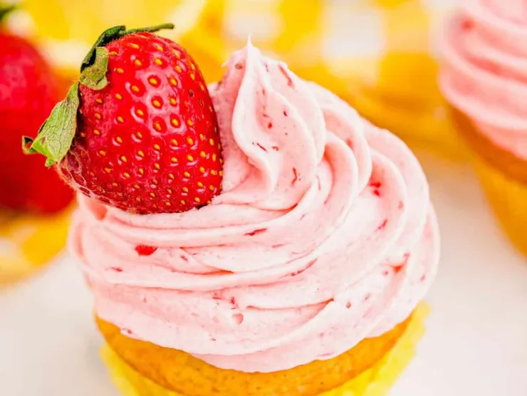 a cupcake with yellow cake and pink icing topped with a whole strawberry