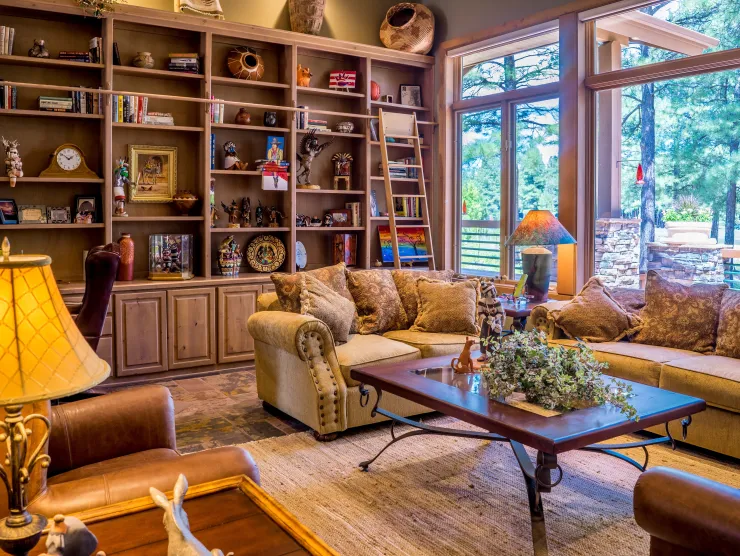 A cozy living room with ambient and natural light, shelves, and large windows.
