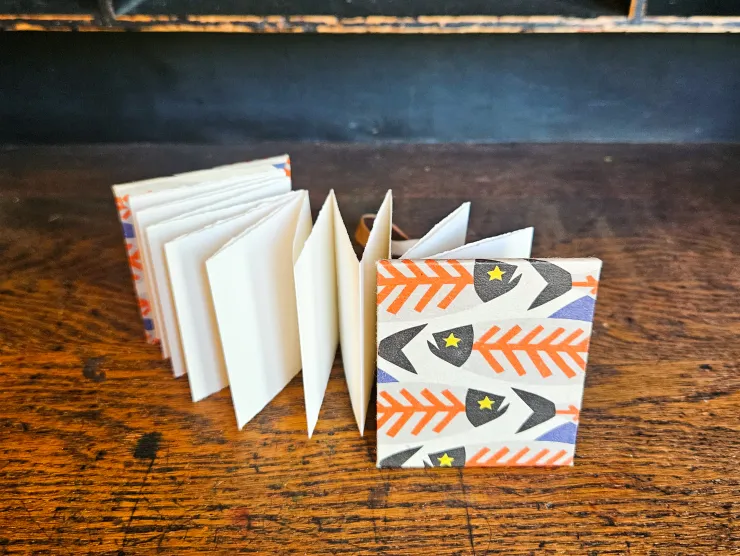 An accordion-style handmade book by Jessica Ream. The cover has orange and grey skeleton fish on it.