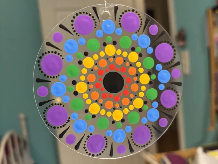 Painted dot mandala in rainbow colors on a clear acrylic disc