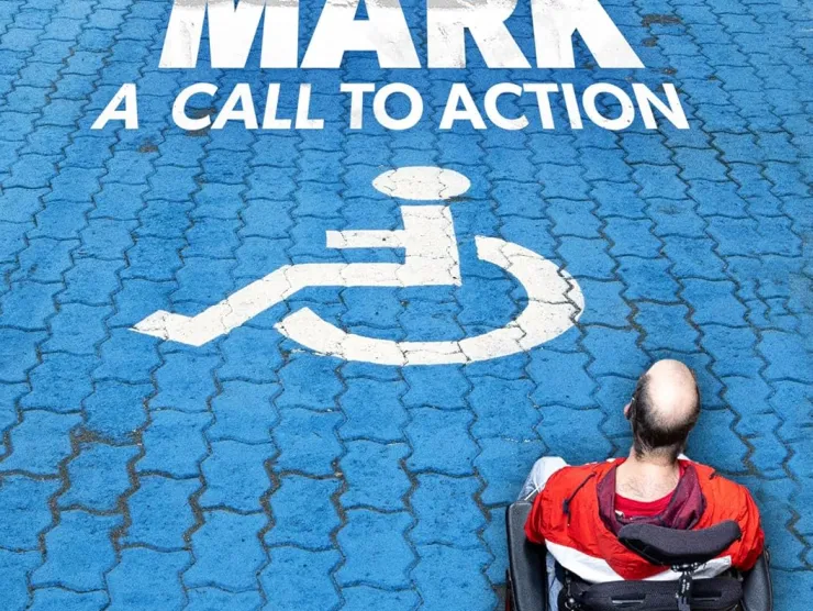 Image of a white man in a wheel chair with his back to the camera.  He is in a blue crosswalk with pavers.  The crosswalk also has the white disability symbol and contains the words:  Mark:  A Call to Action.  The tag line is Imagine a World without Complete Accessibility.   