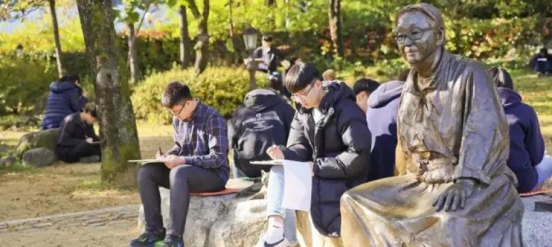 Young people sit on bench by statue of Pak Kyongni