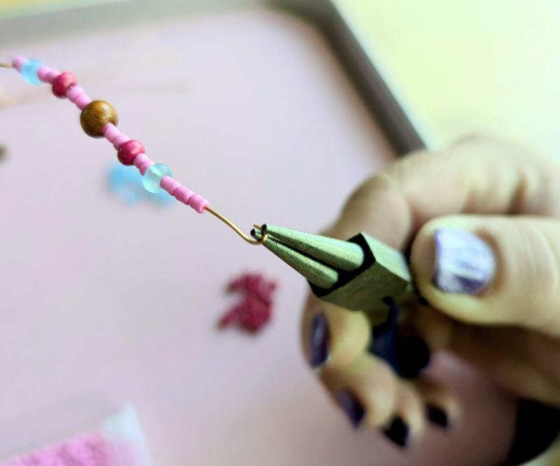 Photo of a person holding a pair of round-nose pliers and curling gold wire around one jaw of them