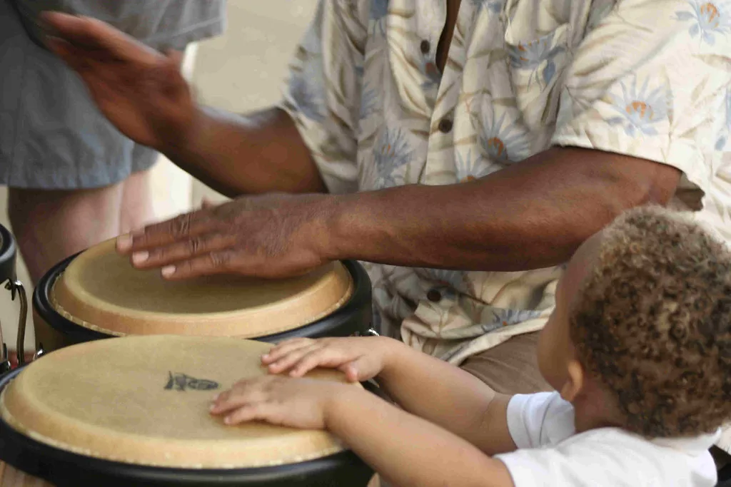 Image of the hands of a man and a young child drumming together.