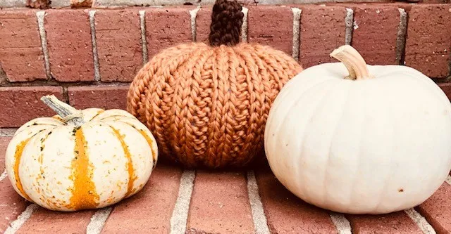 An orange knitted pumpkin and two real pumpkins on a brick step