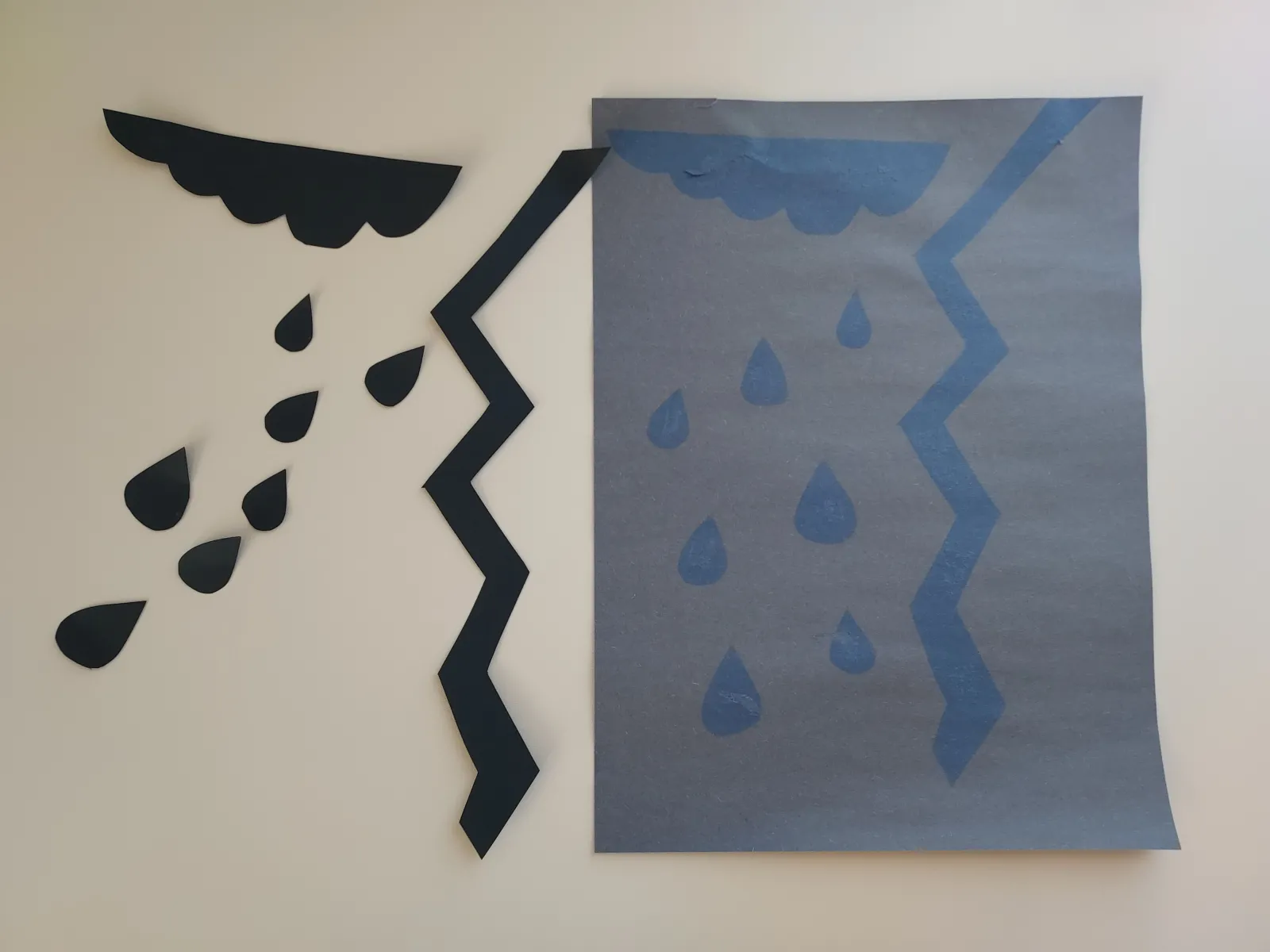 Image of black cardstock cut into a cloud, raindrops, and lightning strike next to the resulting print - a faded background with a blue rainstorm.