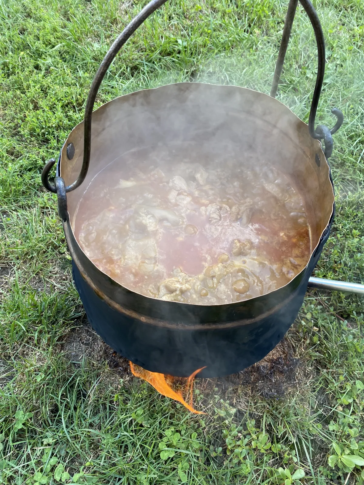 Hungarian gulyás being cooked outside in a traditional metal kettle.