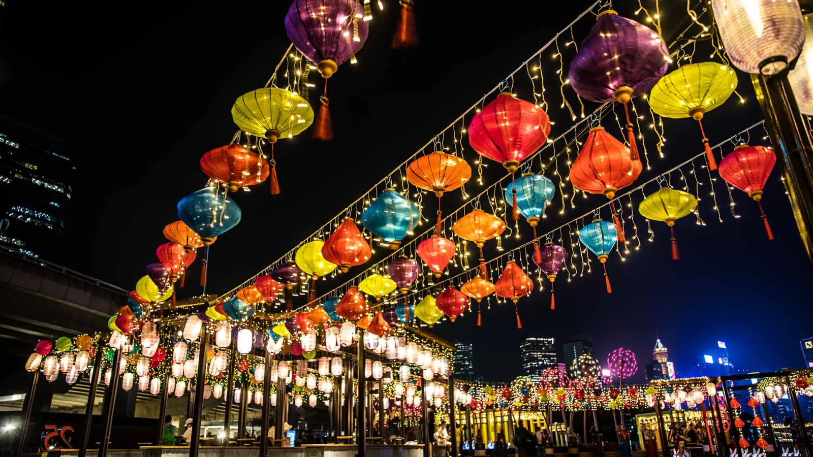 multicolored illuminated paper lanterns hanging against a nighttime city scape