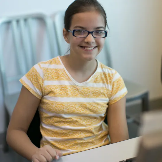 Teen girl with glasses sitting at a desktop computer.