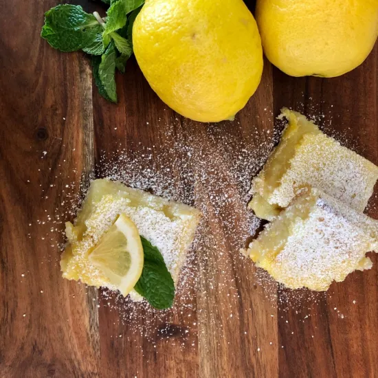 An image of lemons and lemon bar slices on a wooden cutting board