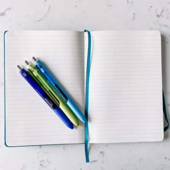 picture of open journal and a dark blue pen, green pen, and light blue pen