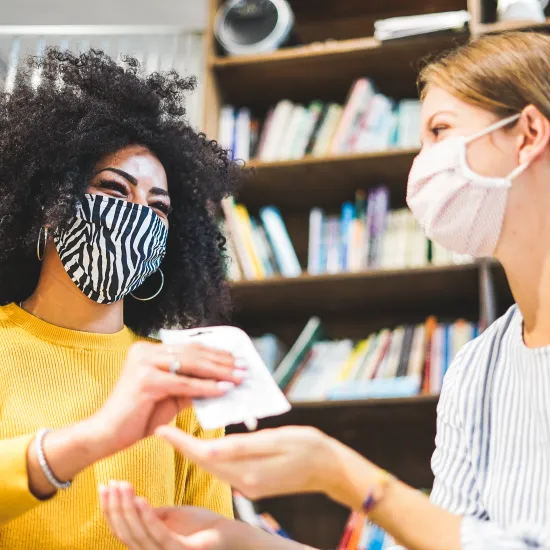 Female library staff member in yellow blouse assists a female customer in a white blouse during the COVID pandemic