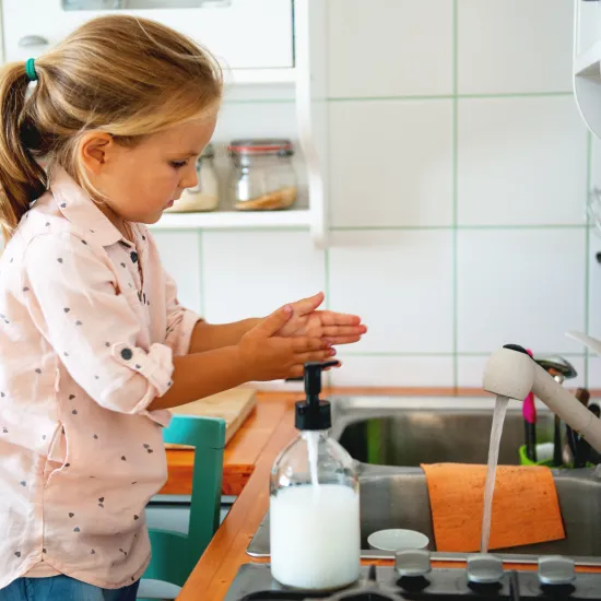 Little girl washes her hands at home in the sink