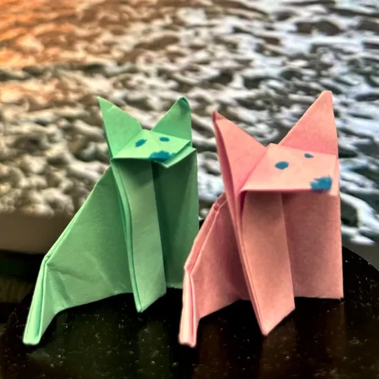 Blue and pink little origami fox dogs in front of photo of sunrise at the beach.