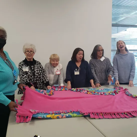 A group of 6 women around a pink felt blanket on a table.