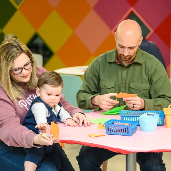 Two adults draw with markers with a toddler