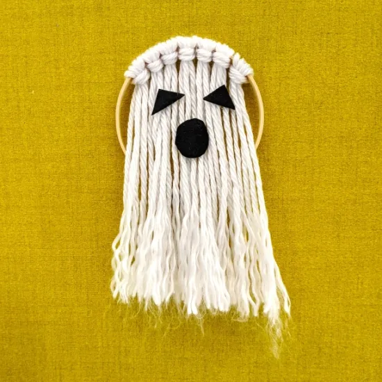 photo: a ghost made of white yarn tied in lark's head knots around an embroidery hoop with black felt eyes and mouth