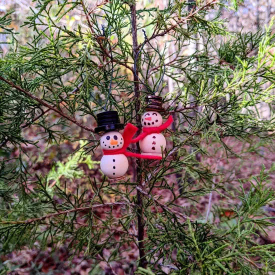 Photo: two snowpeople ornaments made of two wooden beads stacked onto wire with hats and bases made of buttons and felt for scarves