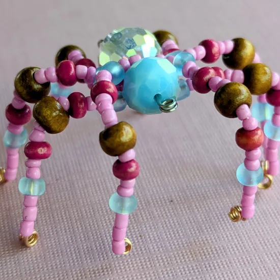 Beaded spider - the head is a light blue faceted bead, the body is a clear faceted bead. The legs are pink, magenta, light blue, and brown beads.